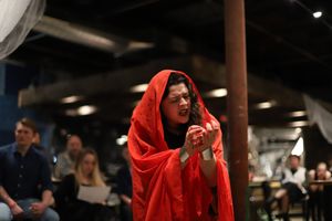 Dramatic scene with performer wearing flowing red cape in theatrical lighting.