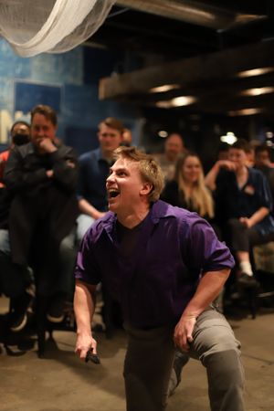 Performer in purple shirt acts expressively during theatrical scene.