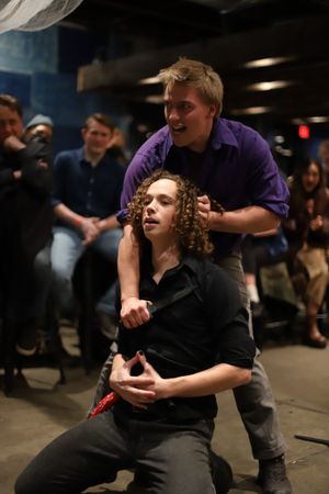 Two performers enact dramatic scene in black and purple costumes.