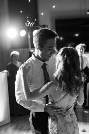 A romantic black and white photo of a couple slow dancing together at an event with soft lighting in the background.