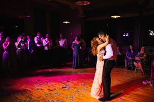 Wedding couple shares their first dance on a lit dance floor surrounded by guests in purple lighting.