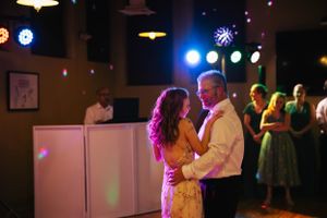 A couple shares an intimate dance moment under colorful party lights on a dance floor.