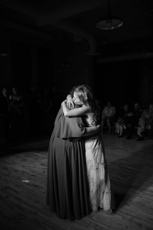 Two figures embrace in an emotional moment on a dimly lit dance floor during a formal event.