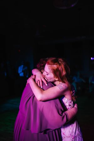 Two people share an emotional embrace on a dark dance floor illuminated by purple lighting.