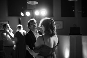 A candid black and white photo captures a couple dancing together under venue lighting.
