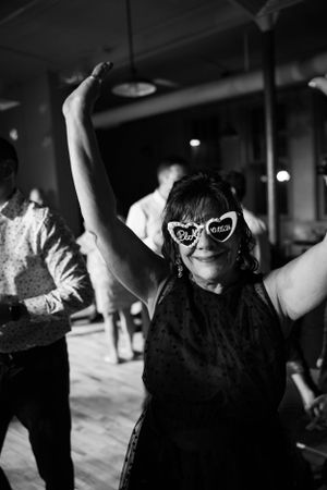 Black and white photo of a dancer wearing heart-shaped sunglasses with arms raised dancing at a party.