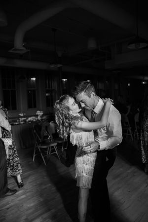 A couple dancing intimately in formal attire on a dimly lit dance floor.