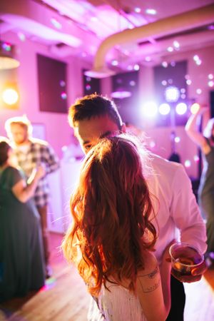 Couple sharing an intimate dance moment at a wedding reception with pink and purple lighting in the background.