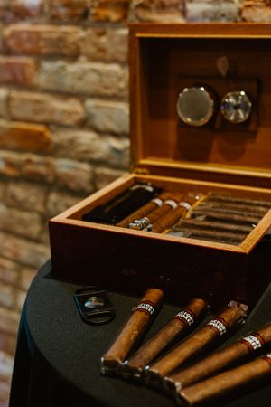 Wooden cigar humidor box displaying premium cigars on a dark surface with exposed brick wall background.
