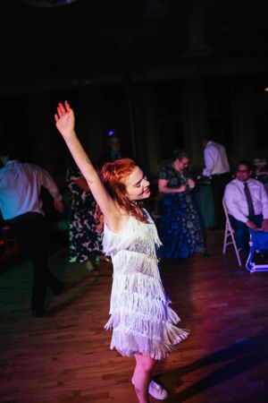 A dancer in a white fringe flapper-style dress twirls energetically on a dimly lit dance floor.
