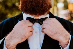 Close-up view of hands adjusting a black bow tie against a white dress shirt in formal attire.