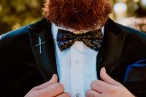 Close-up of a blue bow tie and silver cross necklace worn with a black suit jacket.