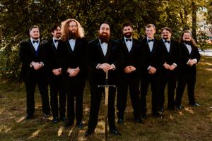 Groomsmen in black tuxedos and bow ties posing formally outdoors for wedding photo.