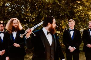 Group of formally dressed groomsmen laughing together outdoors during a wedding photo session.