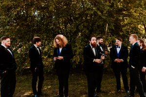 A group of people in formal black suits stand together outdoors having a candid conversation.