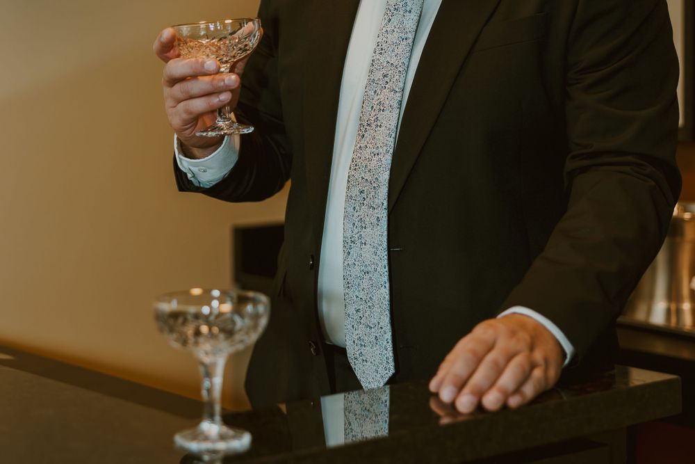 A person in a black suit and light blue tie holds a champagne glass at a formal event.