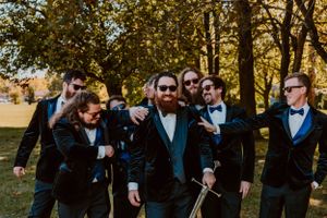 Groomsmen in black suits having fun and laughing together outdoors.