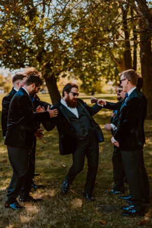 A group of groomsmen sharing a casual moment and laughing together in a sunny outdoor setting.