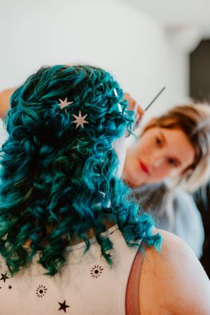 Close-up of vibrant teal curly hair decorated with star accessories.