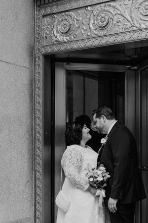A tender moment between newlyweds in a doorway with ornate architectural details, captured in black and white.