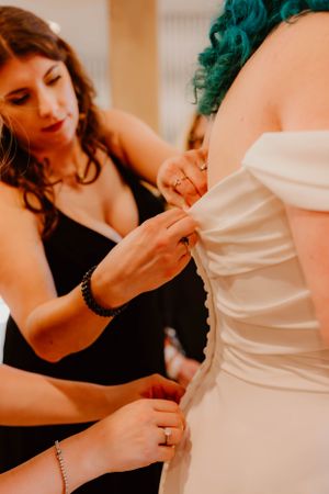 Wedding dress being carefully adjusted and fitted by someone wearing black formal attire.