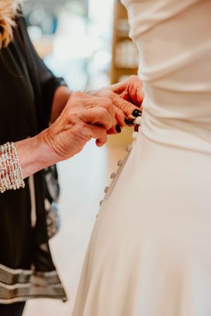 Close-up of hands adjusting a white wedding dress, with one person wearing sparkly bracelets.