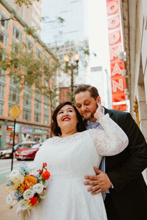 A romantic wedding photo taken in an urban setting with colorful fall flowers and a glowing street sign.