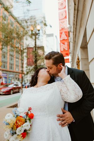 A romantic wedding photo of a couple embracing outside a building with a vintage red sign.