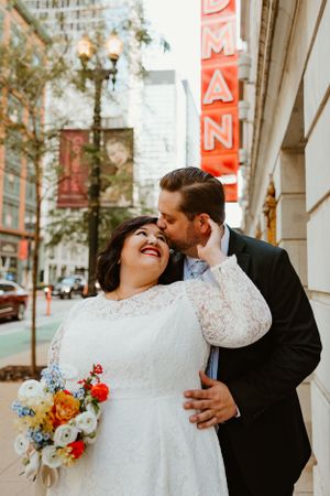 A joyful wedding moment captured outside a city building with a red neon sign.