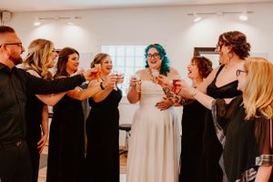 Wedding party in black attire toasting with drinks around someone in a white wedding dress.