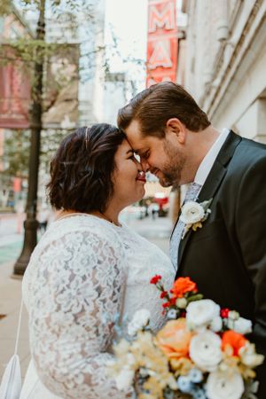A tender wedding moment captured outside a building with pink signage and a beautiful fall bouquet.