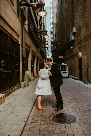 A couple shares a romantic moment in an urban alleyway with vintage brick walls and string lights overhead.