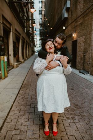 A romantic couple shares an intimate moment in an urban alley with string lights overhead.
