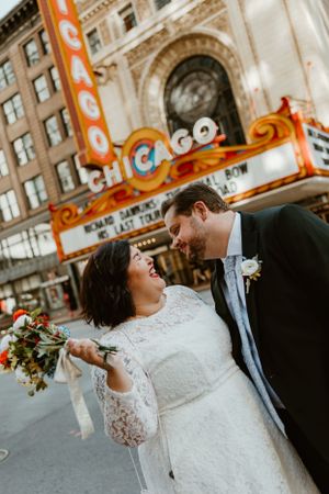 A wedding couple shares a joyful moment outside Chicago's iconic theater marquee with an elegant bouquet.