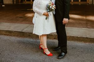 Close-up of a couple's feet and legs, with the bride wearing a short lace dress and red shoes on a city street.