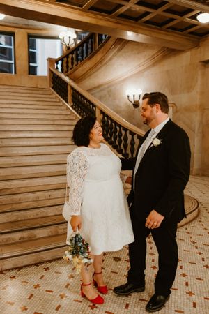A couple shares a romantic moment on an ornate staircase with wood paneling and vintage lighting.