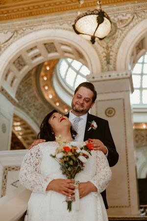 A joyful wedding moment captured in an ornate architectural setting with a beautiful domed ceiling and chandelier.