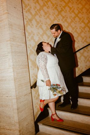 A romantic stairway portrait of newlyweds with vintage lighting and the bride wearing striking red heels.