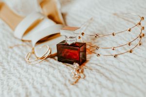 Wedding accessories including delicate hair piece, earrings and red perfume bottle arranged on white fabric.