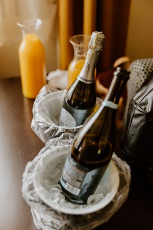 Champagne bottles chilling in ice with orange juice carafes for a celebratory brunch setup.