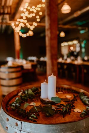 Rustic wine barrel decorated with white candles and greenery under string lights creating a romantic ambiance.