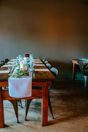 Long wooden dining table set with elegant place settings and simple greenery centerpieces.