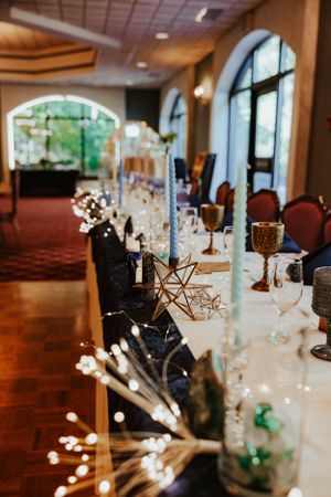 A formal dinner table setup with elegant centerpieces, glassware and geometric decor in an elegant banquet room with arched windows.