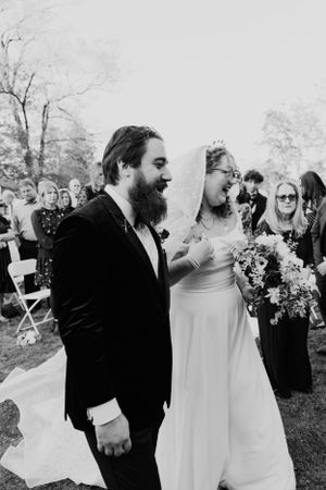 Black and white photo of a bride and groom walking happily together at their outdoor garden wedding ceremony.