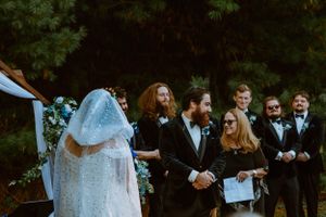 Wedding ceremony in an outdoor garden setting with guests gathered under trees.