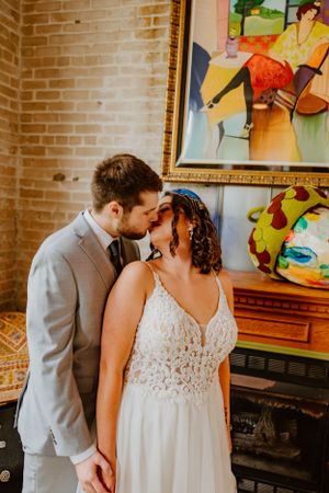 A romantic moment between newlyweds sharing an intimate embrace in front of colorful artwork and exposed brick walls.
