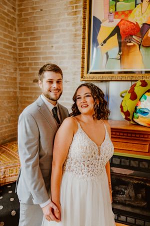 A couple poses in wedding attire against a brick wall with colorful artwork in an indoor setting.