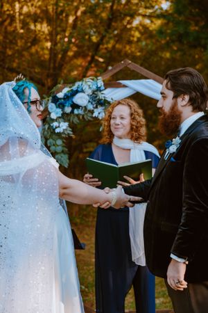 A couple exchanges vows during an autumn outdoor wedding ceremony with blue floral decorations.