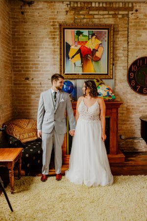 Couple stands in vintage room with brick walls and colorful artwork.