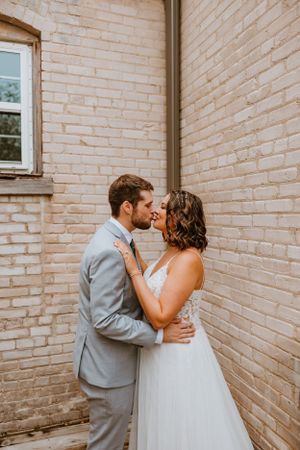 Romantic wedding couple embraces against a rustic brick wall backdrop during their special day.